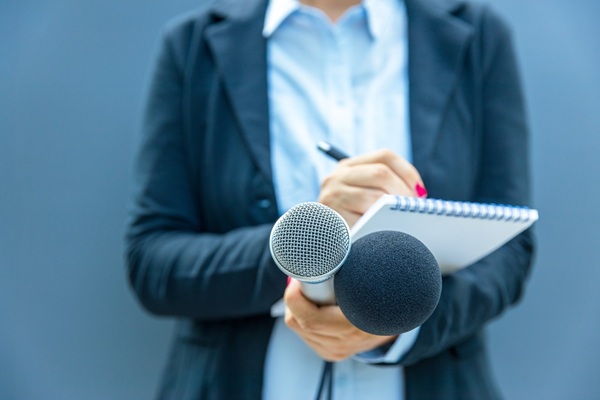 Female,Reporter,Holding,Microphones,And,Writing,Notes,During,Press,Conference,