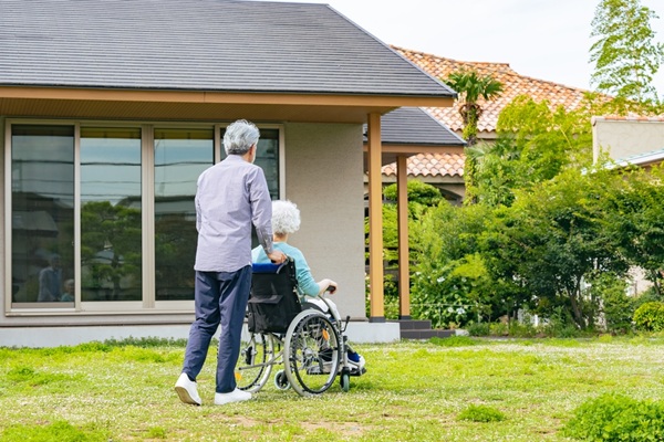 Senior,Couple,In,Wheelchairs,Walking,In,Front,Of,Their,House